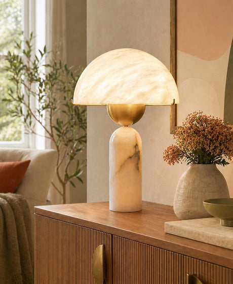 An alabaster table lamp sits on a wooden cabinet; both the shade and the body of this table lamp are crafted from Spanish alabaster, whilst the lamp head is made of brushed gold-coloured copper.