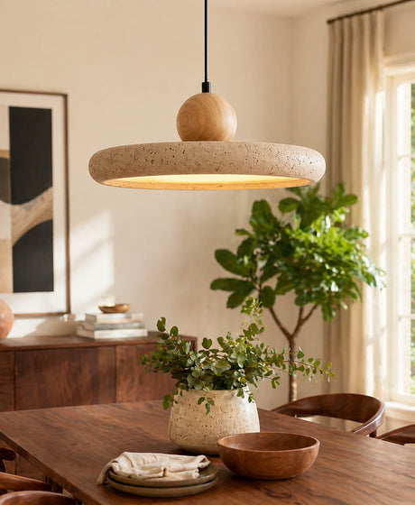 Dining room pendant light fixtures overing wooden table, below of the travertine light is a plant of green leafs.